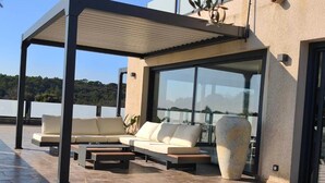 Un espacio moderno al aire libre con sofá y mesa de centro, un jarrón grande y vista al mar.