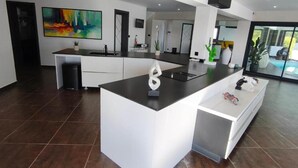 Una cocina moderna con una isla central, muebles blancos y un cuadro abstracto de gran tamaño en la pared.