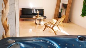Un cuarto de spa con una bañera de hidromasaje, una silla de madera, una mesita y un sofá.
