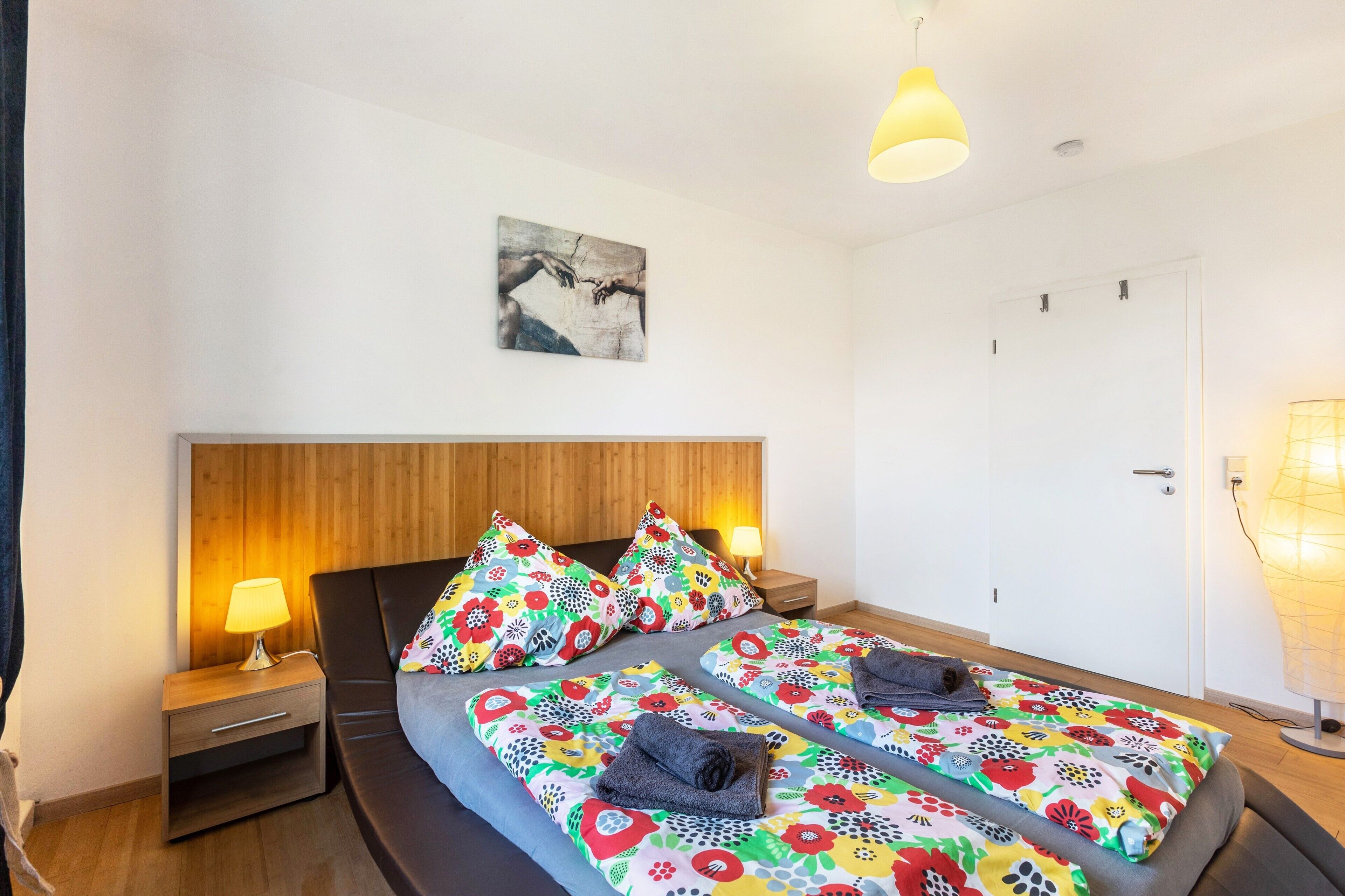 A double bed with floral bedding, a wooden headboard, bedside lamps, and a wall-mounted artwork.