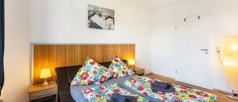 A double bed with floral bedding, a wooden headboard, bedside lamps, and a wall-mounted artwork.