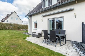 Ett hus med en uteplats som har ett bord och stolar, en liten trädgård och ett hus som ligger intill.