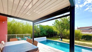 An outdoor pool area with a covered patio, wicker furniture, and a view of the backyard.