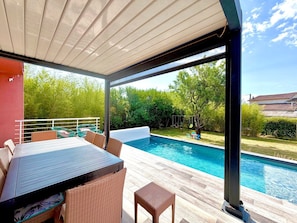 An outdoor pool area with a covered patio, wicker furniture, and a view of the backyard.