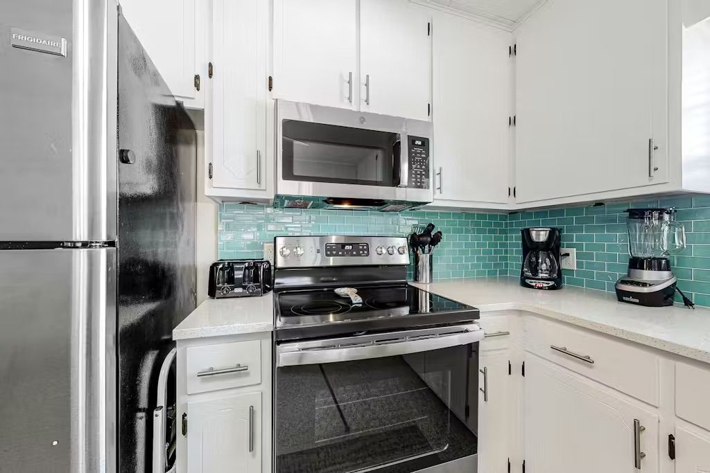 Una cocina con gabinetes blancos, un refrigerador de acero inoxidable, un microondas, una estufa y una cafetera.