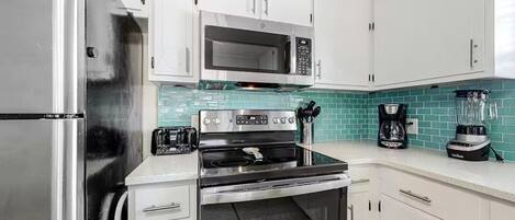 Una cocina con gabinetes blancos, un refrigerador de acero inoxidable, un microondas, una estufa y una cafetera.