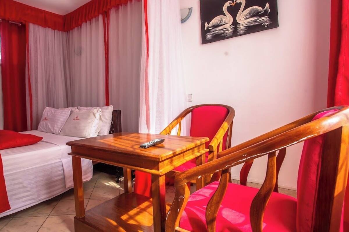 A room with a bed, a wooden table, a red chair, and a painting of swans on the wall.