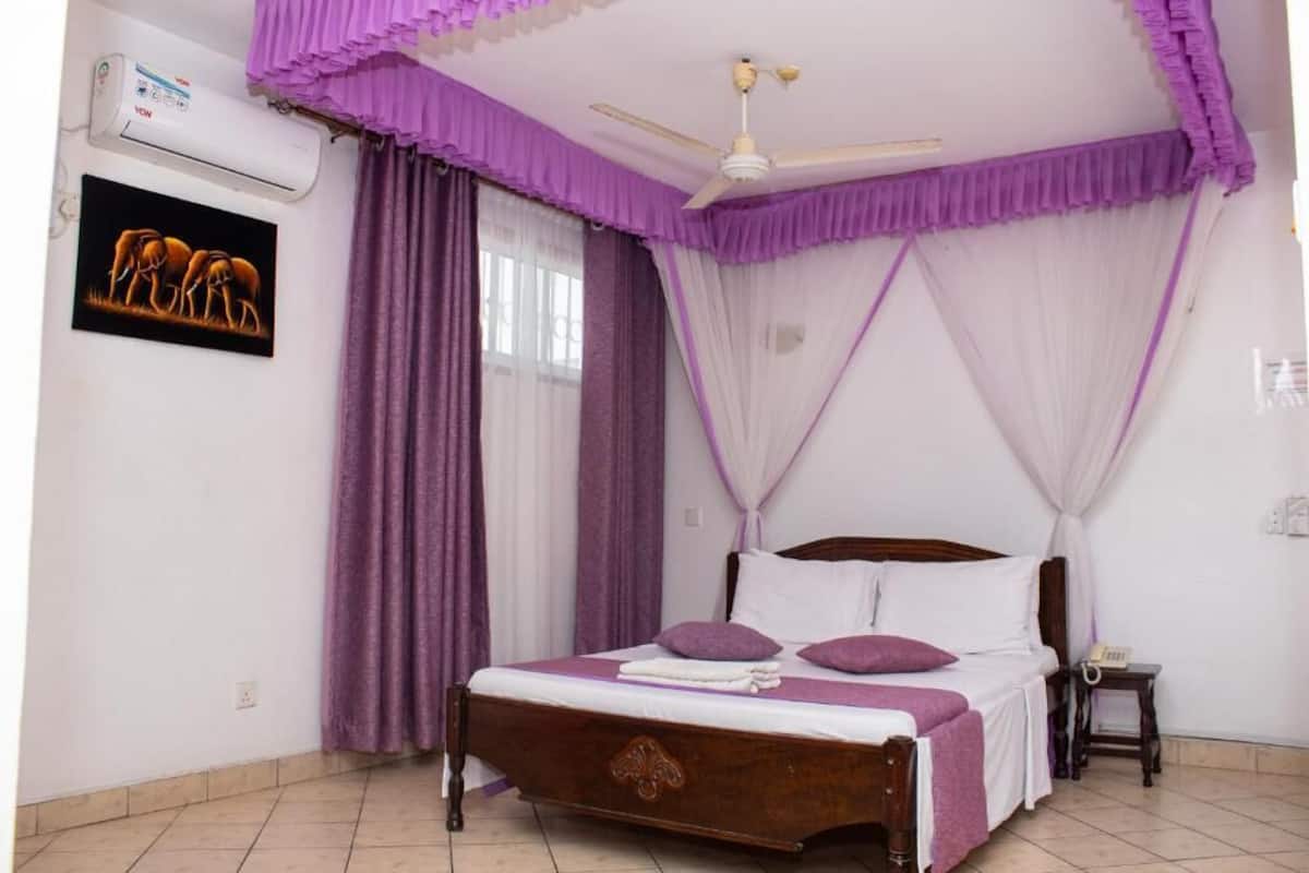 A bedroom with a bed, a ceiling fan, an air conditioning unit, a bedside table, and a wall-mounted picture.