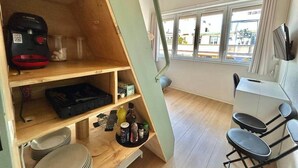 Una habitación compacta con kitchenette, una zona de comedor con sillas y un ventanal que ofrece vistas al exterior.