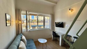Una sala de estar moderna con un sofá, una mesita, un televisor y una escalera.