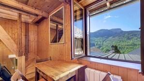 Ein Holzinnenraum mit Tisch und Stühlen, ein Fenster mit Blick auf grüne Hügel.