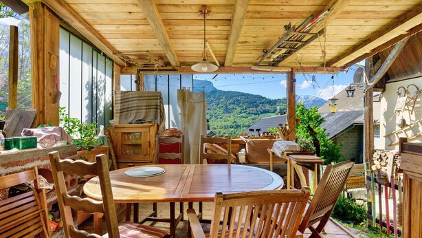 Ein Essbereich mit Holztischen und -stühlen, einer Pendelleuchte und Blick auf eine Berglandschaft.