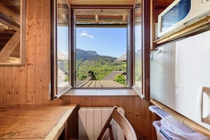 A wooden cabin with a window view of a green landscape and mountains.