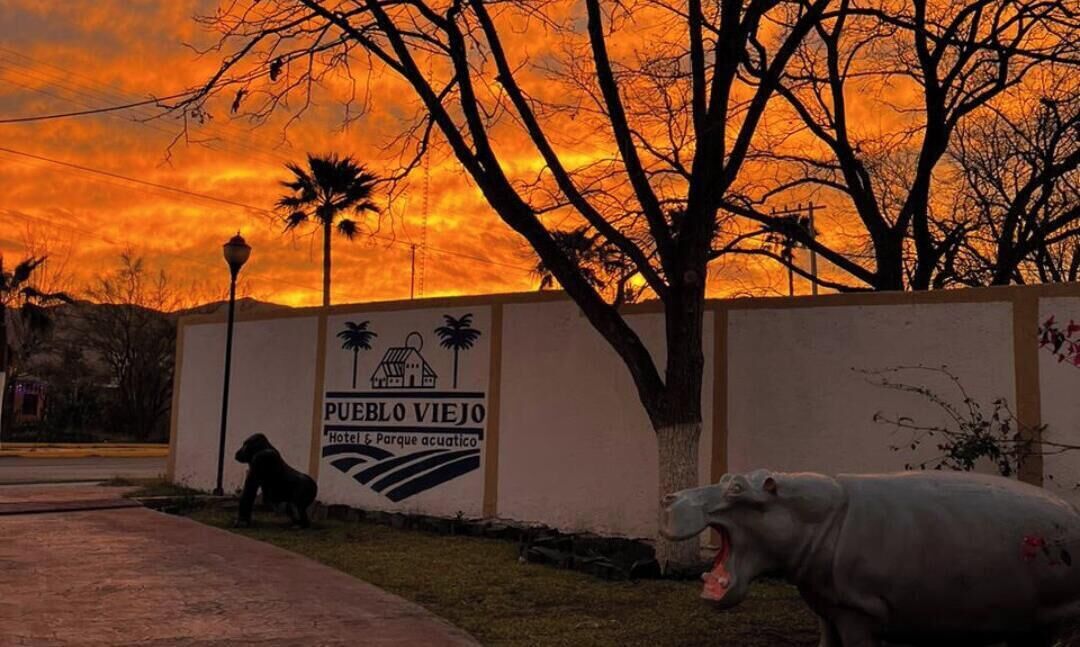 Señal para 'Pueblo Viejo Hotel & Parque acuatico' con un perro y un cerdo al frente.