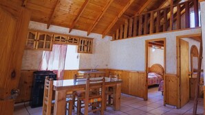 Un intérieur en bois comprenant une table à manger, des chaises, un coin cuisine et une chambre avec un lit.