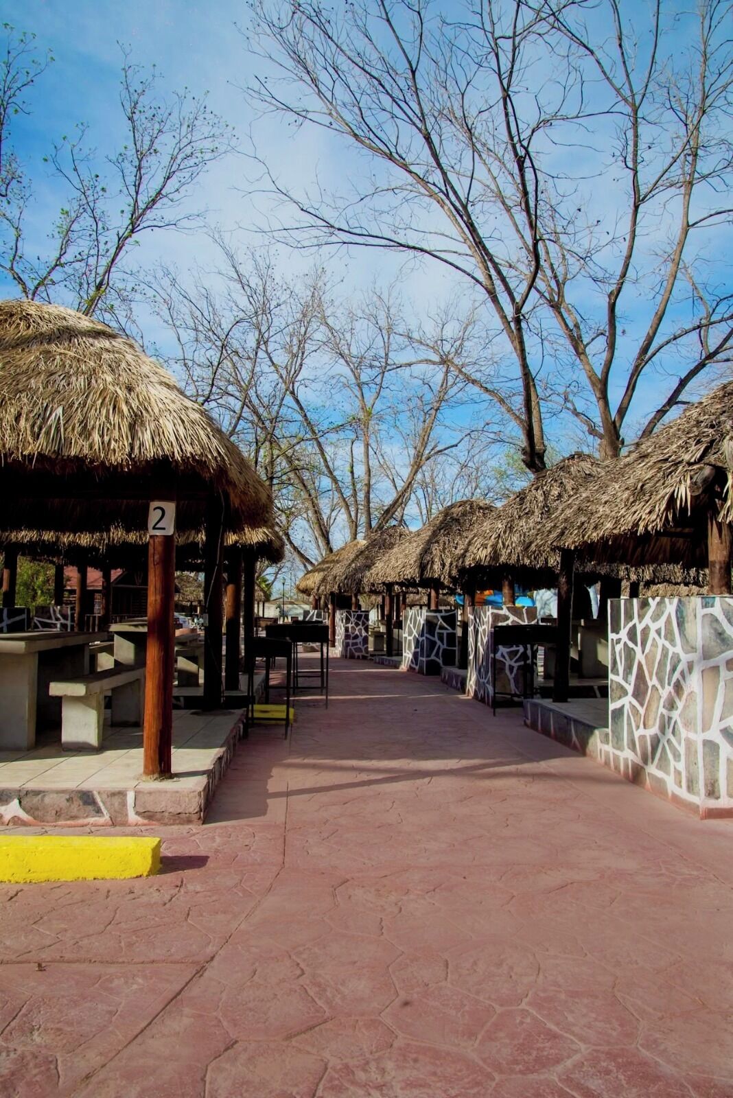 A pathway lined with thatched-roof structures, numbered signs, and stone walls.