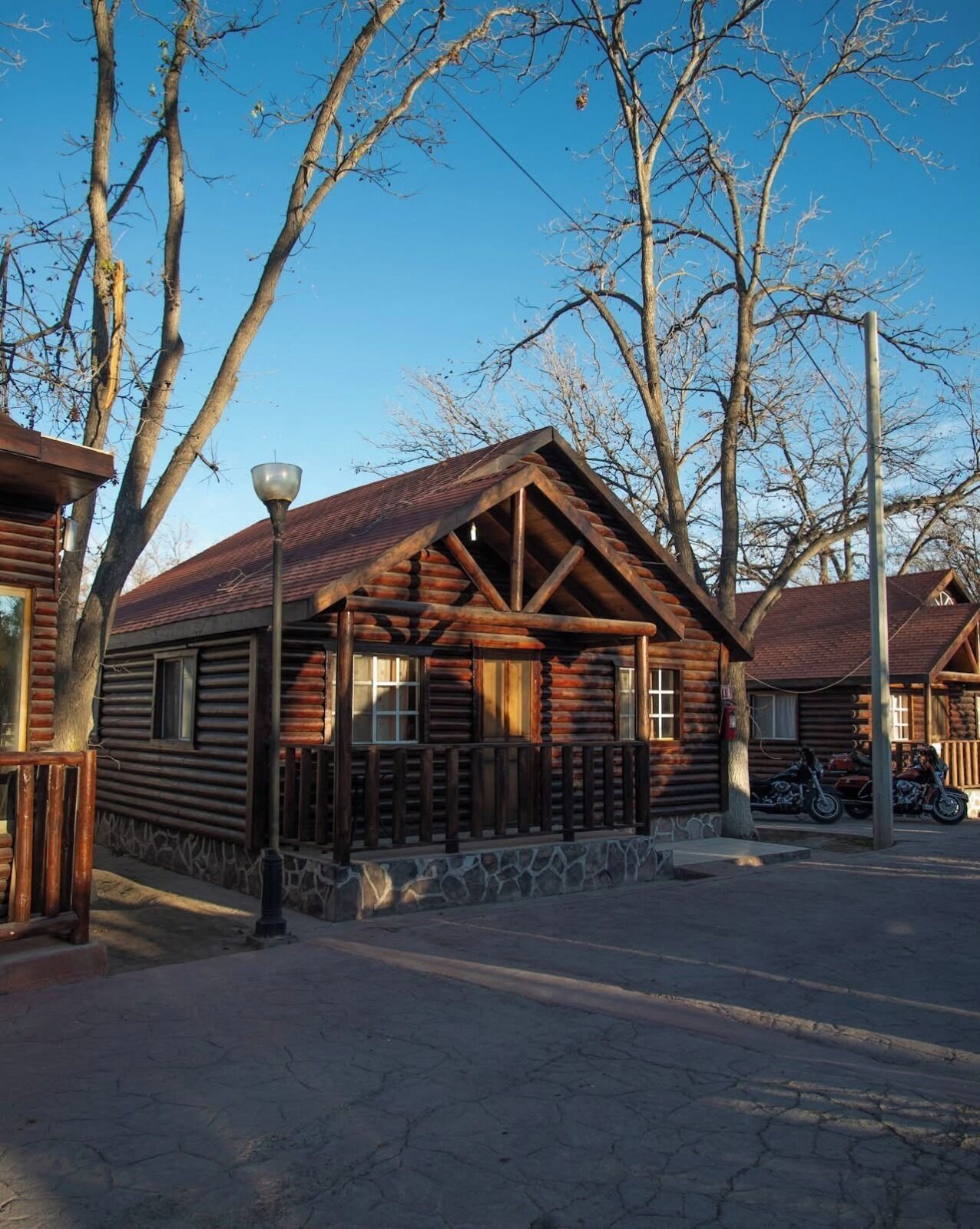 A log cabin with a stone foundation, wooden porch, and a metal lamp post.