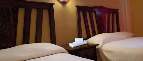 A hotel room with two beds, wooden headboards, a nightstand with a lamp, and a towel on the nightstand.