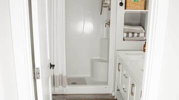 A narrow bathroom with a shower, white cabinets, and a wooden floor.