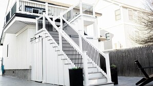 A multi-level residential building with a white exterior, a staircase with black railings, and a wooden fence in the background.