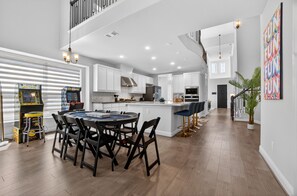 Une cuisine spacieuse équipée d’appareils électroménagers modernes, un coin repas avec une table ronde et des chaises, et un escalier menant à l’étage supérieur.