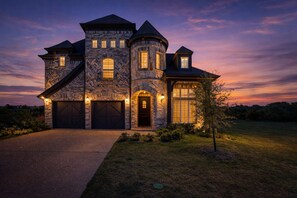 Une grande maison en pierre, dotée de plusieurs portes de garage, d’une tourelle et d’une entrée bien éclairée.