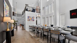 A modern dining area with a long table set for six, a staircase, and a wall-mounted Netflix sign. - Worldcup Ready Luxury 6BR  Game Room  EV  Pets OK  Sleeps 24 (Irving)