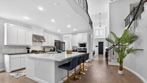 A modern kitchen with white cabinetry, a central island with bar stools, and a staircase leading to an upper level. - Worldcup Ready Luxury 6BR  Game Room  EV  Pets OK  Sleeps 24 (Irving)