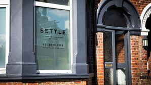 Una ventana con la palabra 'SETTLE' e información de contacto para un establecimiento que ofrece habitaciones y estudios con baño privado de lujo.