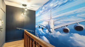 A room with a mural of an airplane flying through clouds, a wooden staircase, and a ceiling light fixture. - Large apartment for 8 people, Sauna & SPA bath, travel around the world (Drusenheim)