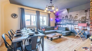A dining area with a table set for six, a sofa, and a director's chair. - Large apartment for 8 people, Sauna & SPA bath, travel around the world (Drusenheim)