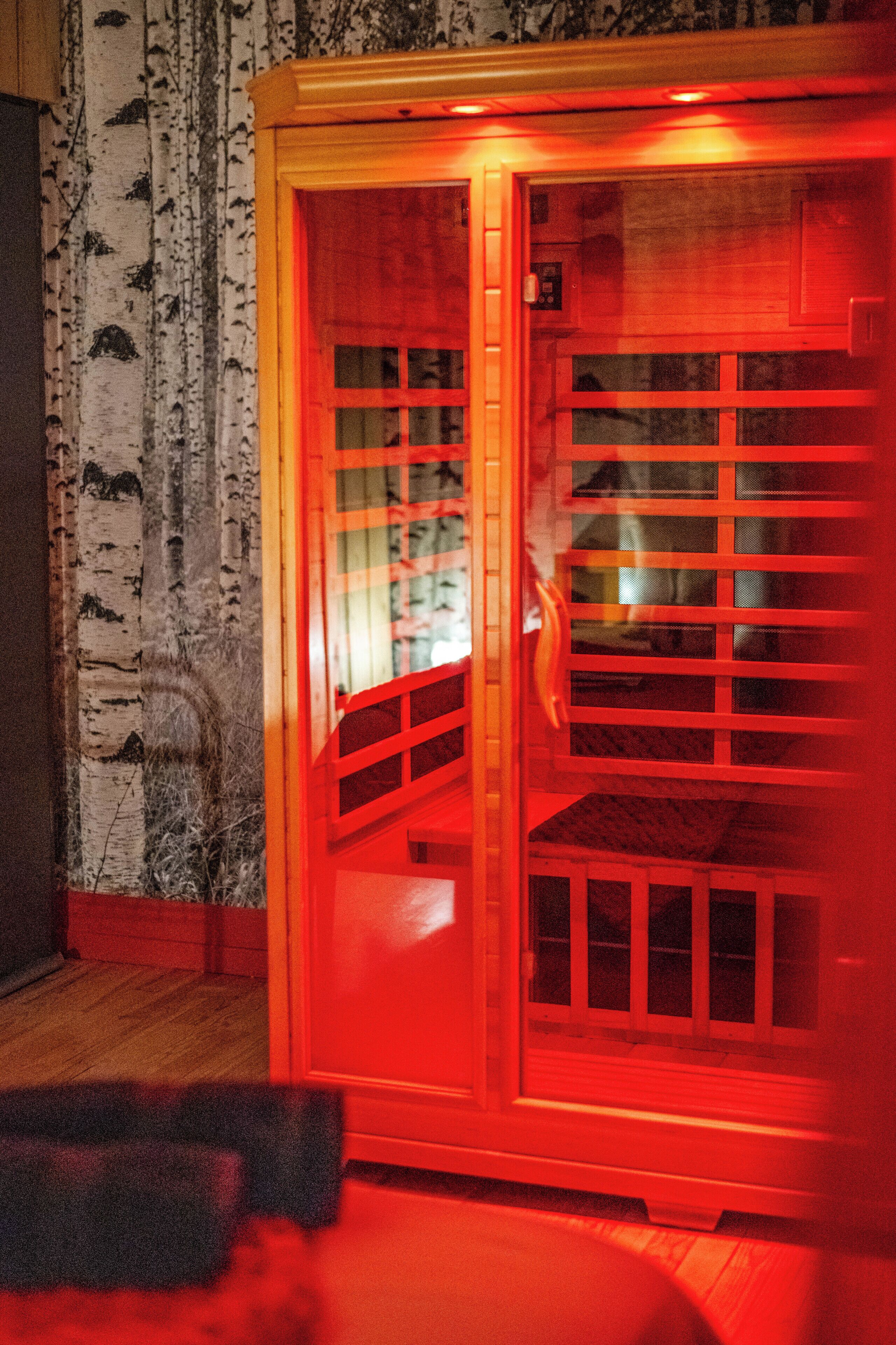 Una sauna con puerta de madera, paneles de vidrio, pared de abedul y suelo de madera.