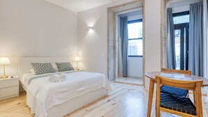 Ein Schlafzimmer mit einem Bett, Nachttischlampen, einem Holzstuhl und einem Fenster mit Vorhängen.