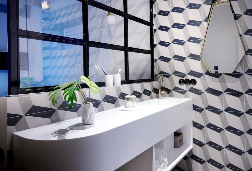 A modern bathroom with a white sink, a potted plant, a mirror, and a geometric patterned wall.