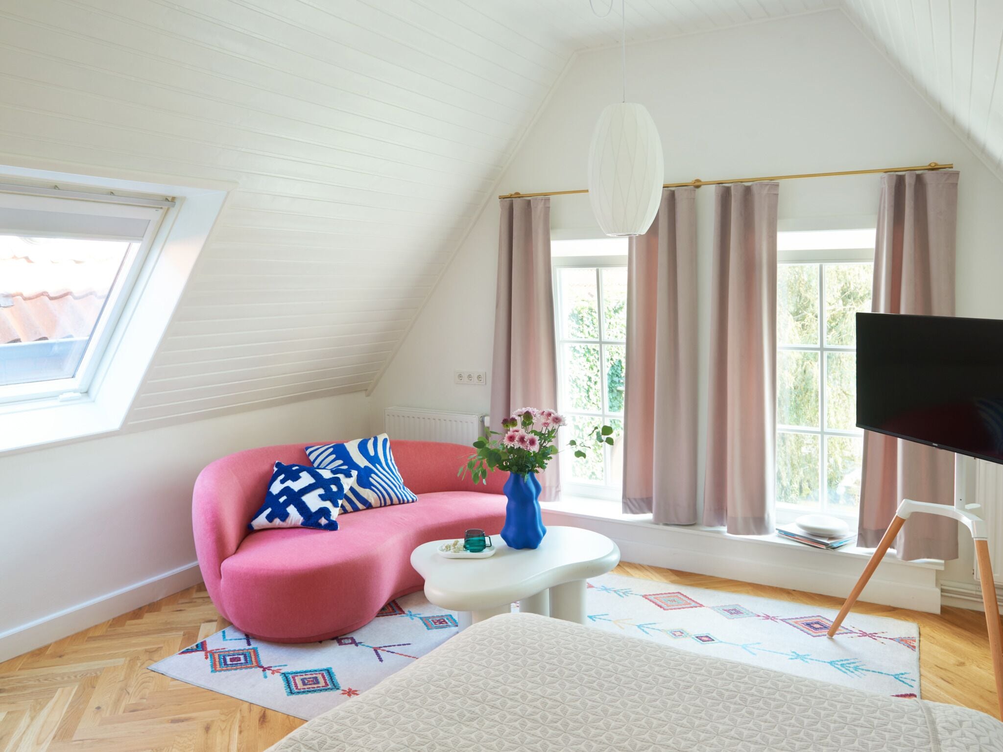 A modern living room with a pink sofa, a white coffee table, a flat-screen TV, and a large window with curtains.