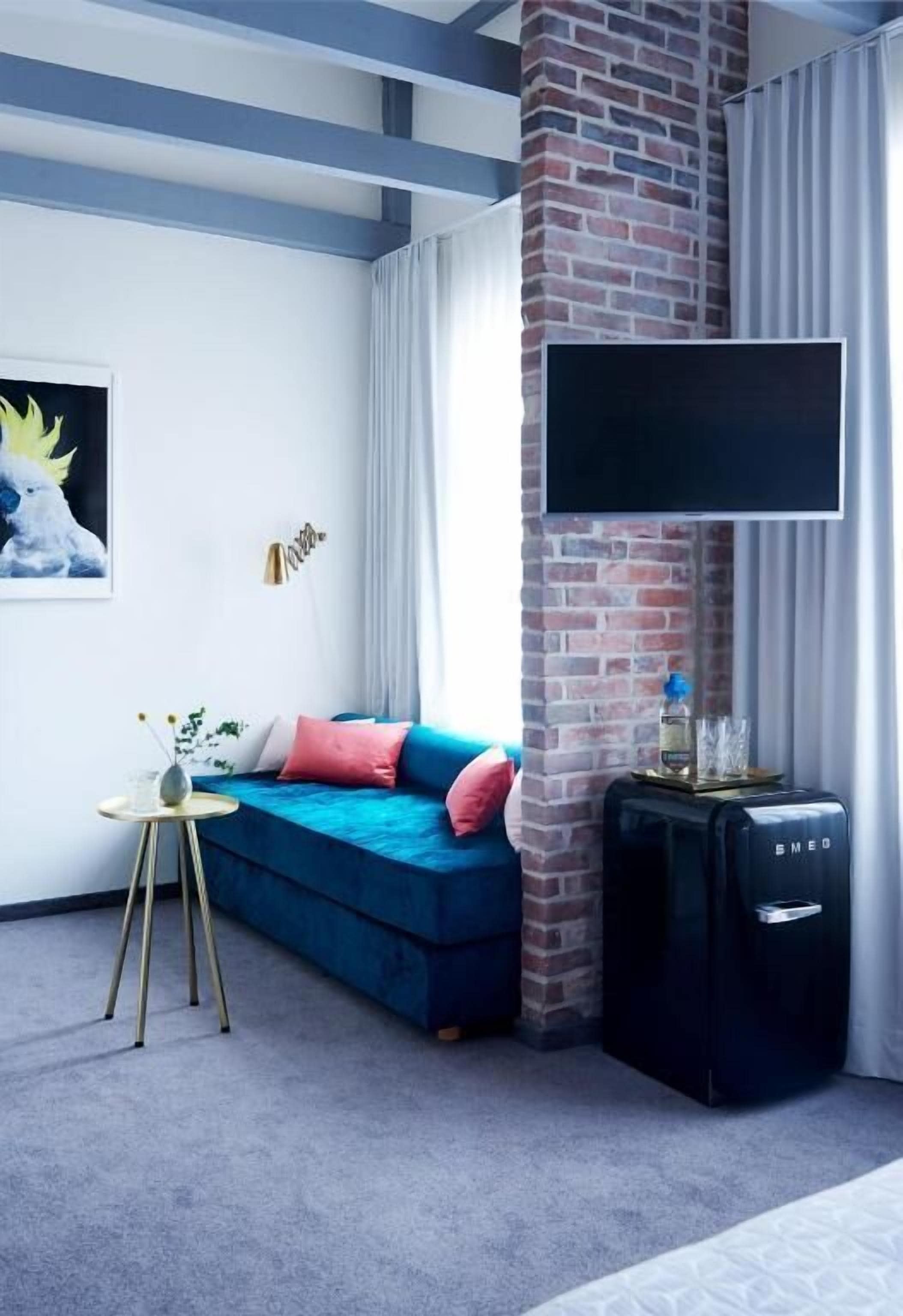 Un salon moderne avec un canapé bleu, un téléviseur à écran plat fixé à un mur en briques, une petite table d’appoint et un haut-parleur noir.