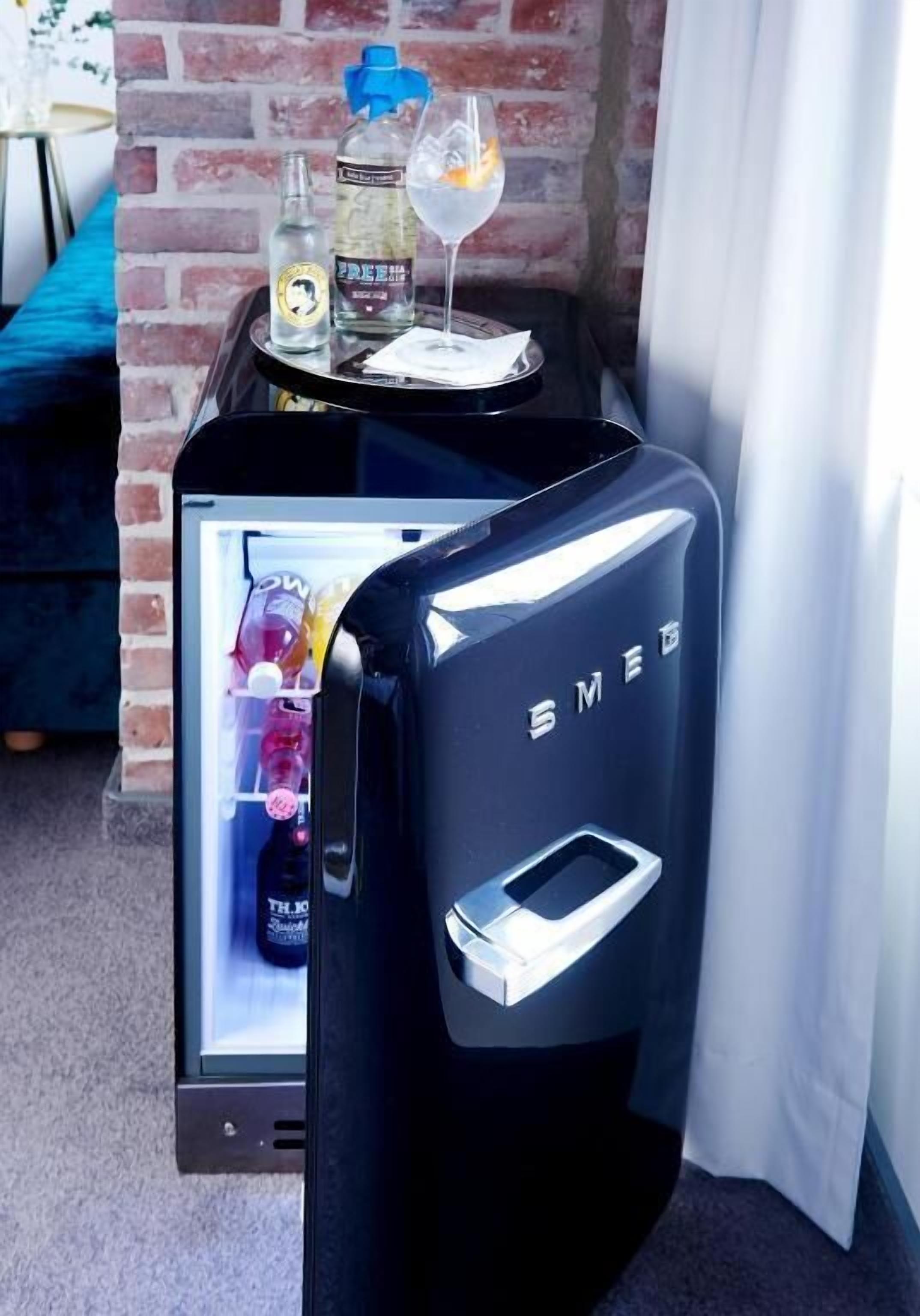 A minibar with a refrigerator, a bottle of water, a bottle of alcohol, and a glass with a drink.