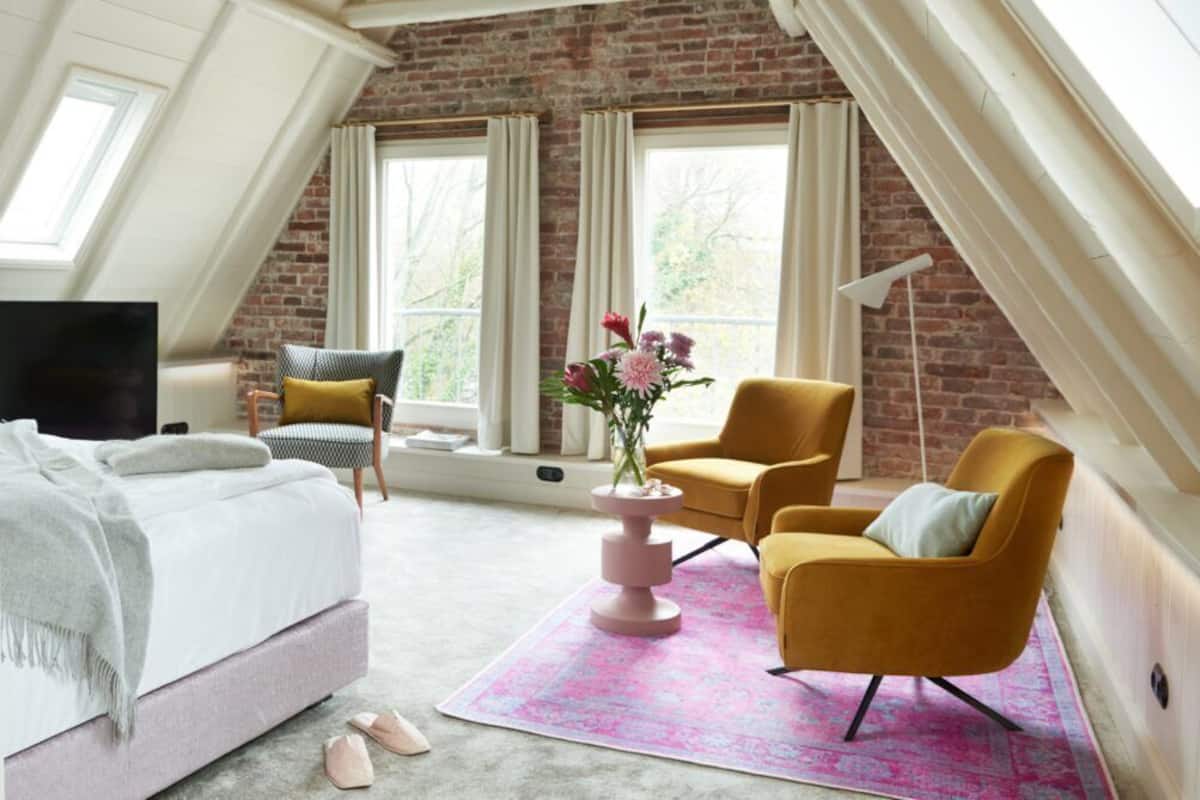 A bedroom with a bed, a chair, a small table with flowers, and a lamp.