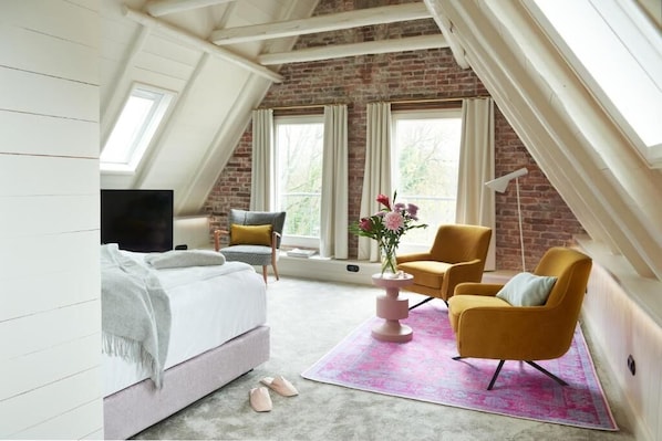 Un dormitorio con una cama, dos sillas, un televisor y una ventana con cortinas.