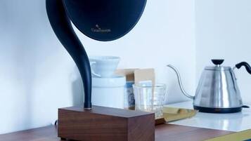 Une cuisine moderne avec une bouilloire noire originale posée sur un support en bois, un meuble bleu et une autre bouilloire en acier inoxydable sur le plan de travail.