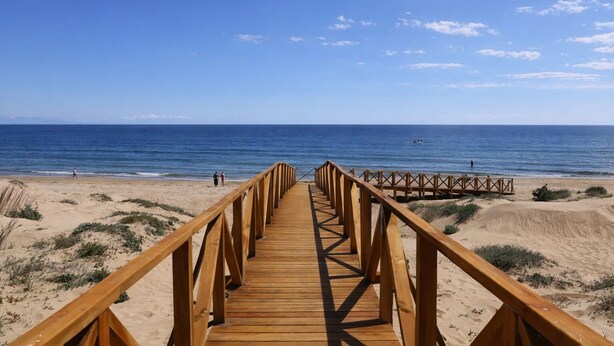 Een houten looppad dat naar een strand leidt, onder heldere luchten.
