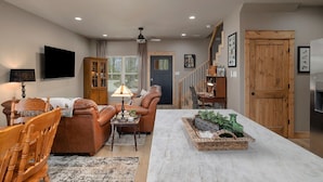 A living room with a sofa, chairs, a coffee table, a TV, and a dining area with a table and chairs. - The Rainbow Trout Cabin, 3-bedroom/2 bath , Dog-friendly, Firepit, Secluded (Cassville)