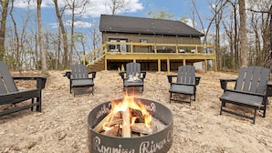 A deck with Adirondack chairs, a fire pit, and a building with a balcony. - The Rainbow Trout Cabin, 3-bedroom/2 bath , Dog-friendly, Firepit, Secluded (Cassville)