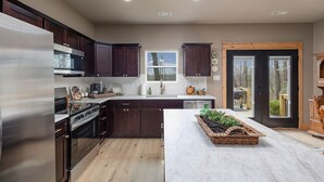 A modern kitchen with dark wood cabinets, stainless steel appliances, and a large island with a woven basket. - The Rainbow Trout Cabin, 3-bedroom/2 bath , Dog-friendly, Firepit, Secluded (Cassville)