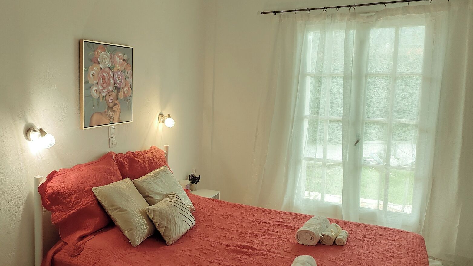 Un lit bien fait, avec des oreillers, un tableau accroché au mur et une fenêtre ornée de rideaux légers.