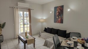 A living room with a sofa, a dining table with chairs, a lamp, and a painting on the wall. - Comfortable Apartment 550m from the Beach with Garden and BBQ (Corfu)