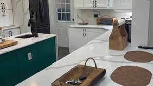 Uma cozinha moderna com armários brancos, uma geladeira preta, um tabuleiro de madeira com chaves e uma luminária pendente.