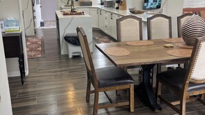 Uma cozinha moderna com arm ários brancos, uma área de jantar com mesa e cadeiras de madeira, e um relógio grande na parede.