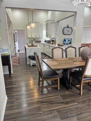 A modern kitchen with white cabinets, a dining area with a wooden table and chairs, and a large clock on the wall. - Lovely 2-bedroom house with AC in tranquil Montego Bay (Montego Bay)