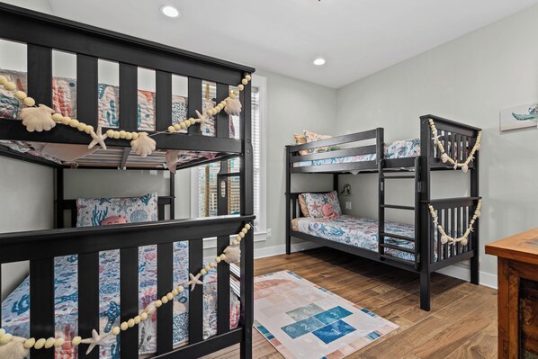 A room with bunk beds, a wooden floor, and a quilted rug. - NEW Family Beachfront Getaway • 4BR on the Sand • Sleeps 12 (Dauphin Island)
